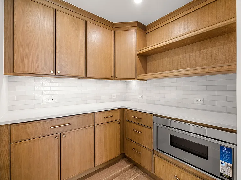 Rift white oak cabinetry with quartz counters and a tiled backsplash by Cambridge Cabinet.