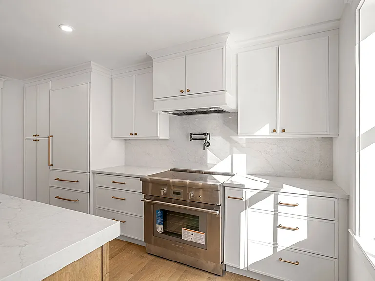 White inset kitchen cabinetry with brass hardware and marble backsplash by Cambridge Cabinet.